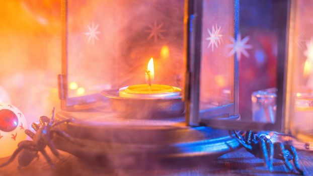 Halloween concept, spooky decorations with lighting up candle and candle holder with blue tone smoke around on a dark wooden table, close up.