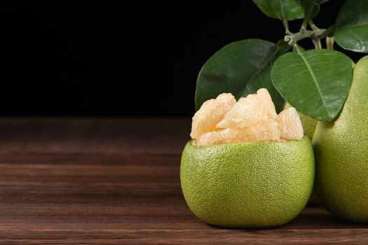 Fresh peeled pomelo, grapefruit, shaddock with green leaves on dark wooden plank table. Seasonal fruit near mid-autumn festival, close up, copy space