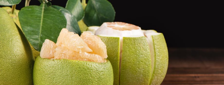 Fresh peeled pomelo, grapefruit, shaddock with green leaves on dark wooden plank table. Seasonal fruit near mid-autumn festival, close up, copy space