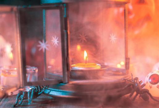 Halloween concept, spooky decorations with lighting up candle and candle holder with green tone smoke around on a dark wooden table, close up.