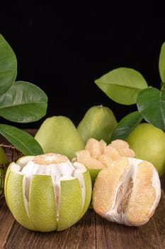 Fresh peeled pomelo, grapefruit, shaddock with green leaves on dark wooden plank table. Seasonal fruit near mid-autumn festival, close up, copy space