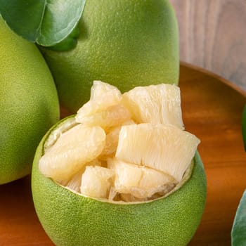 Fresh peeled pomelo, grapefruit, shaddock with green leaves on dark wooden plank table. Seasonal fruit near mid-autumn festival, close up, copy space