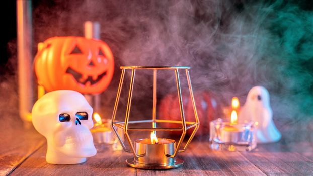 Halloween concept, spooky decorations with lighting up candle and candle holder with green tone smoke around on a dark wooden table, close up.