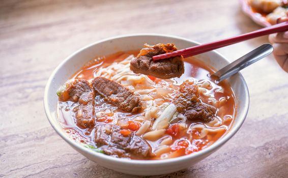Beef noodle - Taiwan ramen meal with tomato sauce broth in bowl on bright wooden table, famous chinese style food, close up, top view, copy space