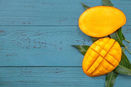 Fresh mango - beautiful chopped fruit with green leaves on dark blue timber background. Tropical fruit design concept. Flat lay. Top view. Copy space