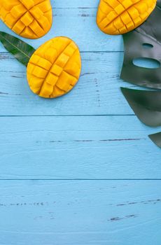 Fresh mango - beautiful chopped fruit with green leaves on bright blue timber background. Tropical fruit design concept. Flat lay. Top view. Copy space