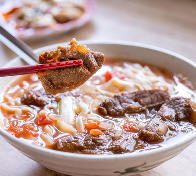 Beef noodle - Taiwan ramen meal with tomato sauce broth in bowl on bright wooden table, famous chinese style food, close up, top view, copy space