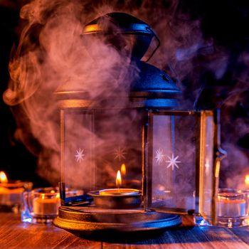 Halloween concept, spooky decorations with lighting up candle and candle holder with blue tone smoke around on a dark wooden table, close up.