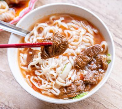 Beef noodle - Taiwan ramen meal with tomato sauce broth in bowl on bright wooden table, famous chinese style food, close up, top view, copy space