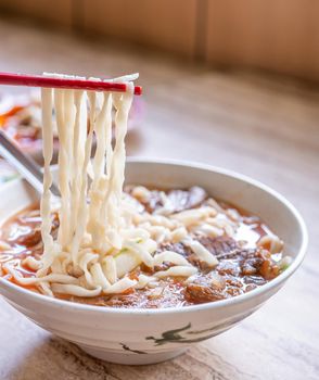 Beef noodle - Taiwan ramen meal with tomato sauce broth in bowl on bright wooden table, famous chinese style food, close up, top view, copy space