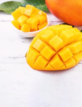 Beautiful chopped mango chunks with green leaves on bright white color timber background. Copy space, close up, macro. Tropical fruit concept.