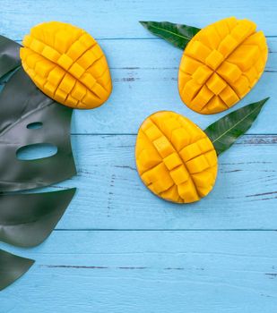 Fresh mango - beautiful chopped fruit with green leaves on bright blue timber background. Tropical fruit design concept. Flat lay. Top view. Copy space