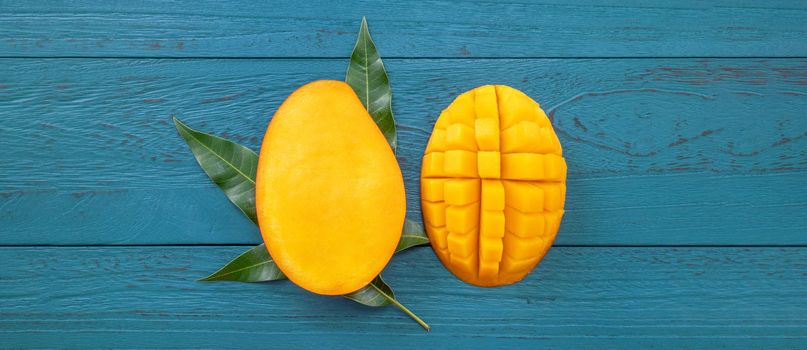Fresh mango - beautiful chopped fruit with green leaves on dark blue timber background. Tropical fruit design concept. Flat lay. Top view. Copy space