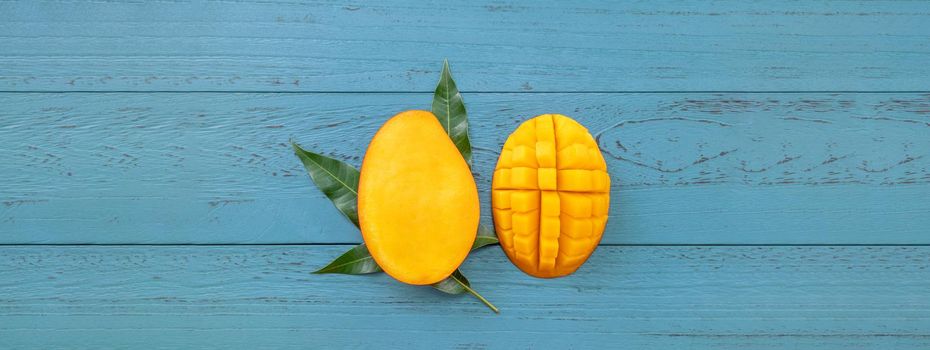 Fresh mango - beautiful chopped fruit with green leaves on dark blue timber background. Tropical fruit design concept. Flat lay. Top view. Copy space