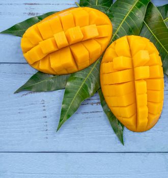 Fresh mango - beautiful chopped fruit with green leaves on bright blue timber background. Tropical fruit design concept. Flat lay. Top view. Copy space