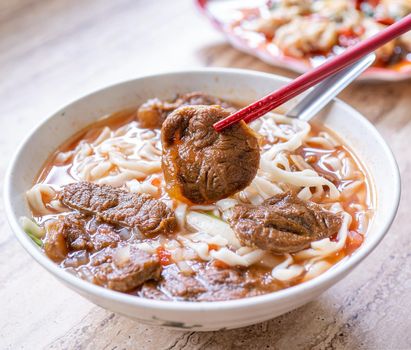 Beef noodle - Taiwan ramen meal with tomato sauce broth in bowl on bright wooden table, famous chinese style food, close up, top view, copy space