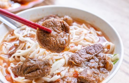 Beef noodle - Taiwan ramen meal with tomato sauce broth in bowl on bright wooden table, famous chinese style food, close up, top view, copy space