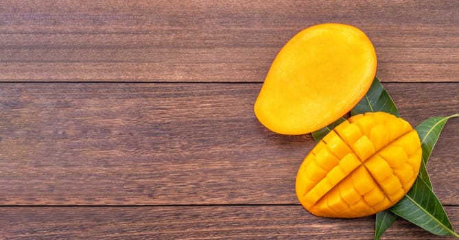 Fresh mango - beautiful chopped fruit with green leaves on dark wood background. Tropical fruit design concept. Flat lay. Top view. Copy space.