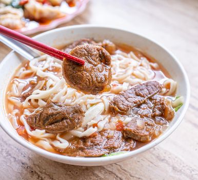 Beef noodle - Taiwan ramen meal with tomato sauce broth in bowl on bright wooden table, famous chinese style food, close up, top view, copy space
