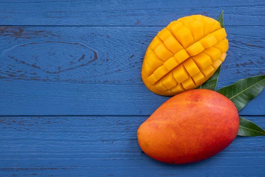 Fresh mango - beautiful chopped fruit with green leaves on dark blue timber background. Tropical fruit design concept. Flat lay. Top view. Copy space