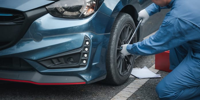 Close up of Young mechanic cropped hand of fixing tire with wearing blue uniform. Car mechanic squatting next to the car in the auto repair shop. Mature man holding changing car wheel.