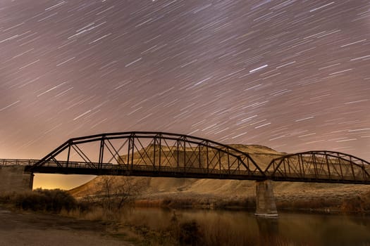 star trails on a bridge with the night sky lit up