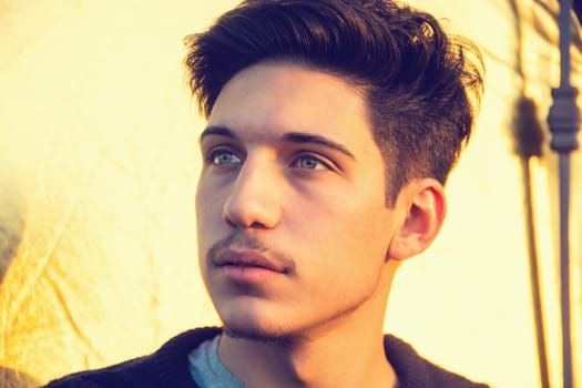 Headshot of one handsome young man with green eyes, looking away to a side, outdoor in a sunny day