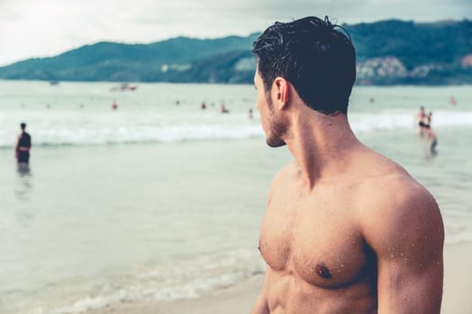 Half body shot of a handsome young man standing on a beach in Phuket Island, Thailand, shirtless wearing boxer shorts, showing muscular fit body