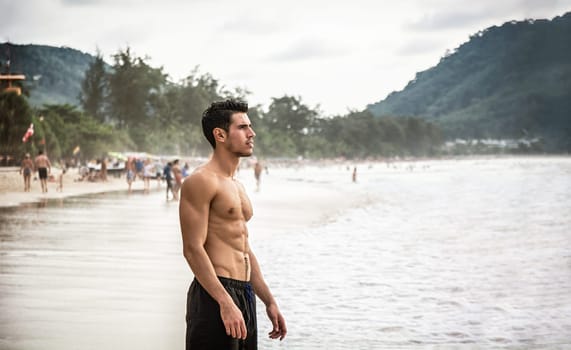 Half body shot of a handsome young man standing on a beach in Phuket Island, Thailand, shirtless wearing boxer shorts, showing muscular fit body