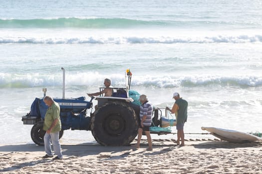 24 April 2023 Lisbon, Portugal: a man on a tractor pulls a fishing net along the shore. Mid shot