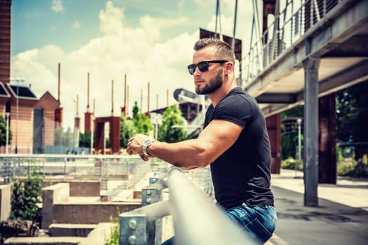 Handsome muscular athletic man in city park during the day, wearing black t-shirt