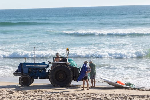 24 April 2023 Lisbon, Portugal: men fishers on the seashore - one of them sitting on a tractor. Mid shot