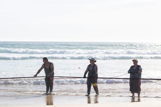 24 April 2023 Lisbon, Portugal: fishermen on the shore pull big fishing net out of the sea. Mid shot