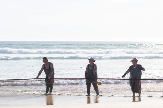 24 April 2023 Lisbon, Portugal: several fishermen on the shore pull big fishing net out of the sea. Mid shot
