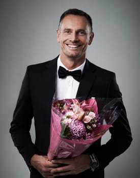 Portrait, man and bouquet of flowers, suit and happiness for Valentines day, romance and on grey studio background. Face, male and guy with floral gift, smile and gesture for love, romantic and happy.