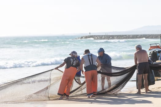 24 April 2023 Lisbon, Portugal: several fishermen on the shore pull out fishing net out of the sea. Mid shot