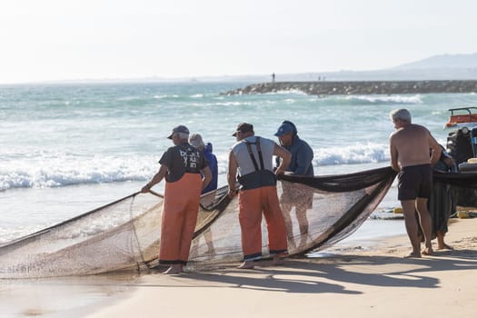 24 April 2023 Lisbon, Portugal: fishermen on the shore pull out fishing net out of the sea. Mid shot