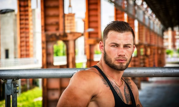 Handsome muscular athletic man in city park during the day, wearing black tank top