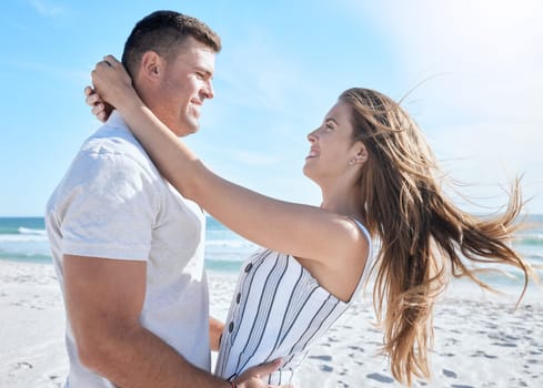 Love, beach and summer with a couple hugging on the sand by the sea or ocean while on holiday together. Happy, smile and romance with a man and woman bonding while on vacation or break by the water.