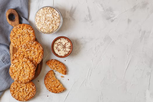 Oatmeal cookies with sesame seeds and flax seeds on a gray background with a jar of oatmeal and textiles. copy space