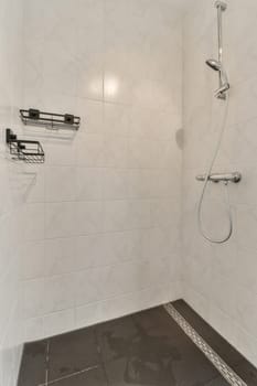 a shower room with white tiles and black flooring on the walls, there is a hand held shower head