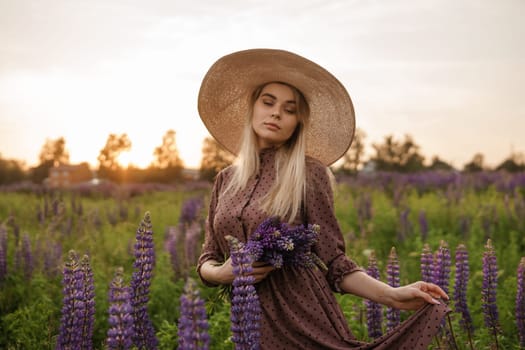 A beautiful woman in a straw hat walks in a field with purple flowers. A walk in nature in the lupin field.