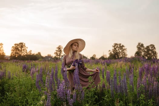 A beautiful woman in a straw hat walks in a field with purple flowers. A walk in nature in the lupin field.