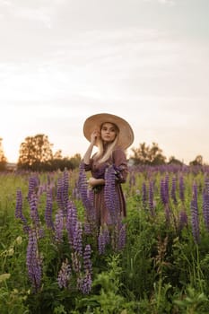 A beautiful woman in a straw hat walks in a field with purple flowers. A walk in nature in the lupin field.