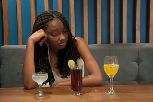 bored afro girl looking at 3 cocktail glasses on a table. High quality photo