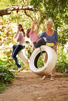 Grandmother, garden and grandkids playing with senior woman on tyre swing or holiday and having fun in summer. Excited, grandchildren and outdoors on jungle gym together or on sunny weekend at a park.