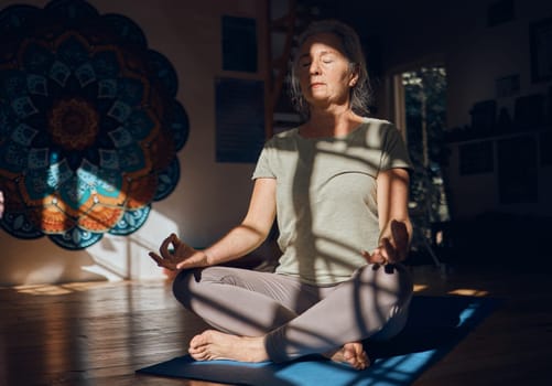 Yoga, prayer hands and meditation of senior woman in dark house for spiritual wellness alone. Chakra energy, zen or mature female training in home to relax with eyes closed for mindfulness or peace