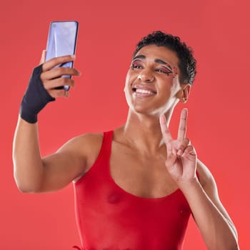 Selfie, queer and gay man peace sign gesture for social media update isolated against a studio red background. LGBTQ, non binary and gen z fashion model with online photo for the internet.