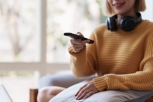 Young woman watching TV resting on sofa sitting in living room in house. Female watch film on television sitting on couch in apartment, leisure.