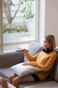 Young woman watching TV resting on sofa sitting in living room in house. Female watch film on television sitting on couch in apartment, leisure.